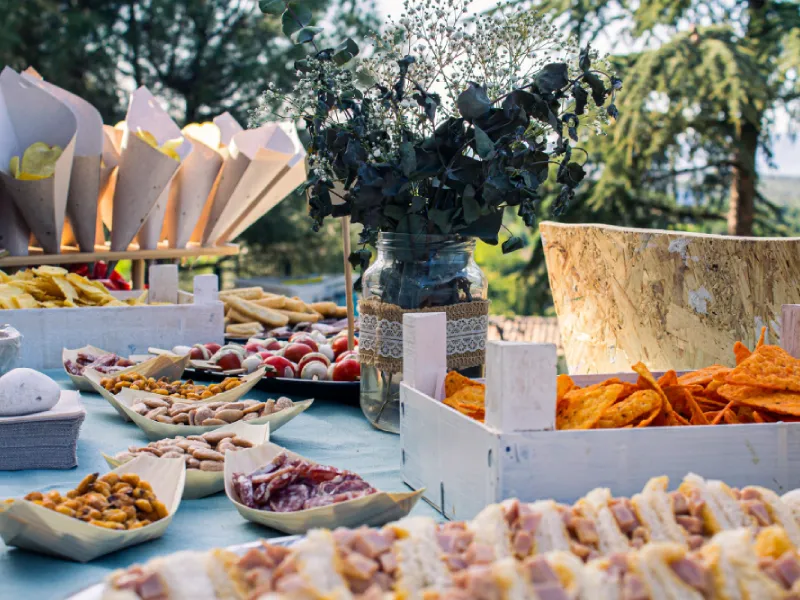 An outdoor buffet with prepared dishes, folded napkins and glassware.