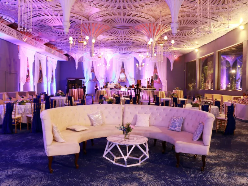 White lounge seating and reception tables in a venue lit with purple light.