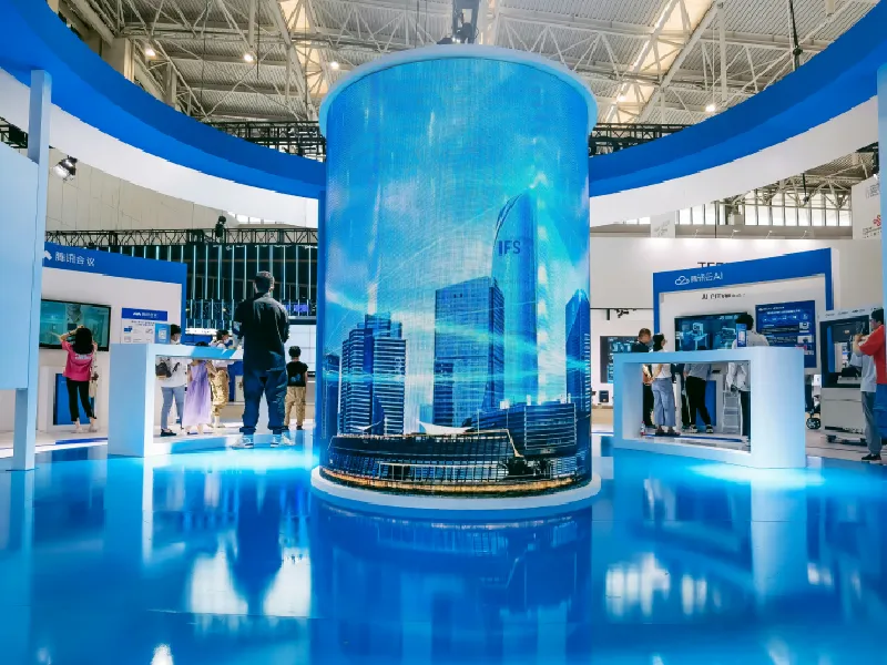 A blue cylindrical exhibition display surrounded by stands inside a large hall.