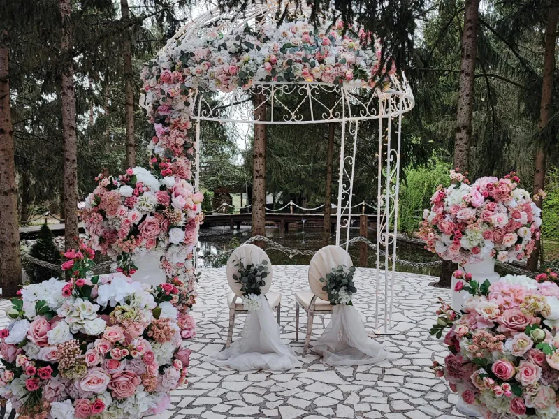 A white garden ceremony structure surrounded by pink and white flowers.